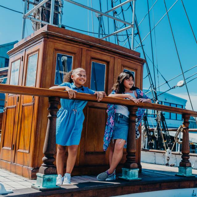 two children look over a boat railing at the Seaport Museum on a sunny day in Galveston