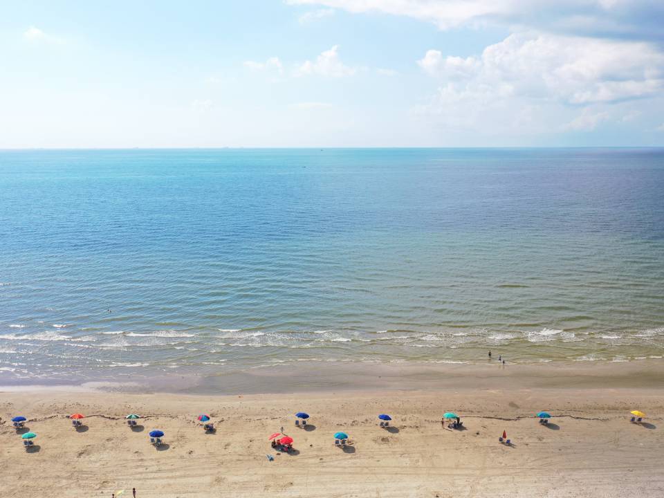 Aerial view of beachgoers at Stewart Beach on Galveston Island, TX. It is a bright, sunny day and waves are rolling to shore