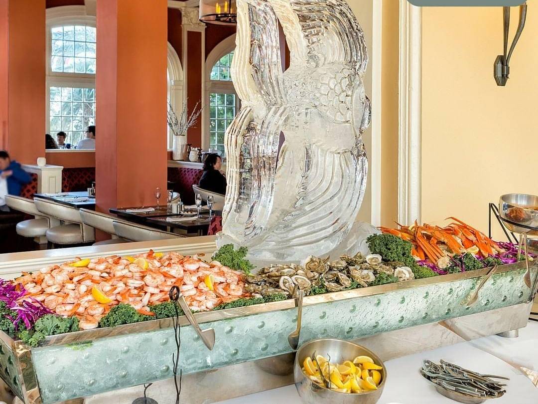 A fish ice sculpture in a tray of shrimp, oysters, and crab legs, at Grand Galvez Thanksgiving brunch
