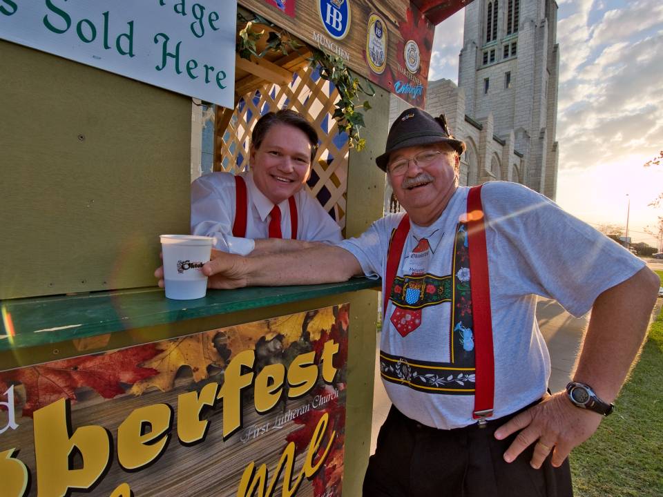 Two men standing at beer booth dressed in traditional German attire at the Island Oktoberfest event in Galveston TX