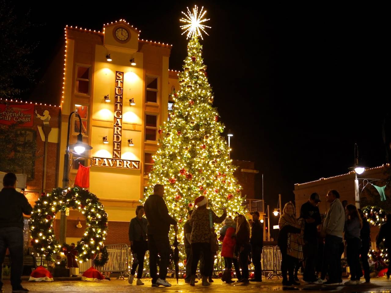 people gather around an illuminated christmas tree and holiday wreath in Downtown Galveston