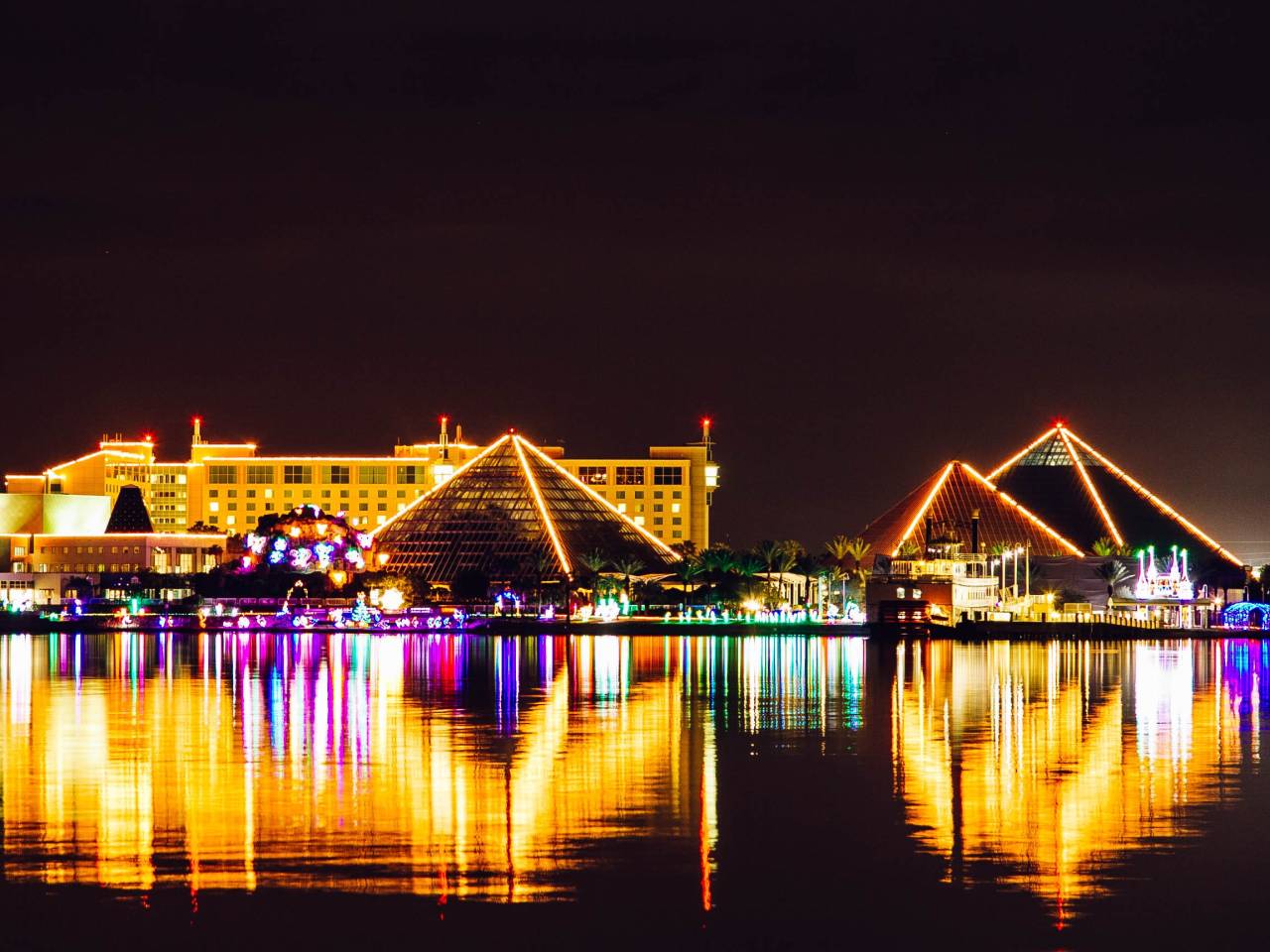 the three Moody Gardens pyramids outlined in holiday lights reflect off of the water