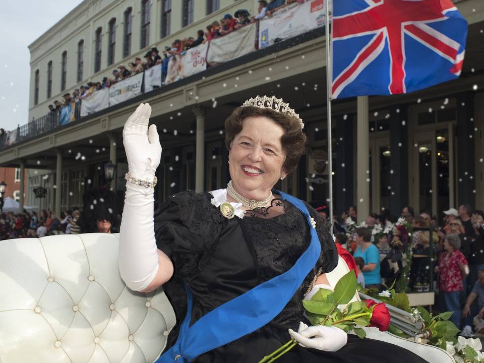 A woman dressed as a queen sits in a carriage holding roses during the Dickens on the Strand Galveston parade.