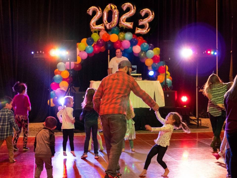 adults and children dance on a dance floor in front of decorative 2023 balloons