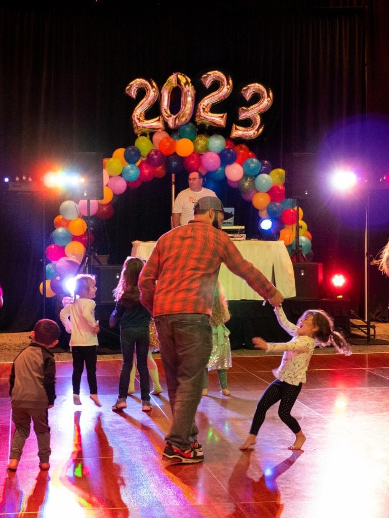 adults and children dance on a dance floor in front of decorative 2023 balloons