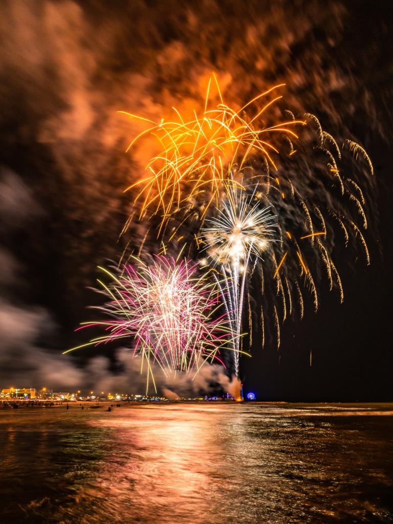 orange, red, and white fireworks light up the Gulf during a 4th of July fireworks display over the beach in Galveston TX