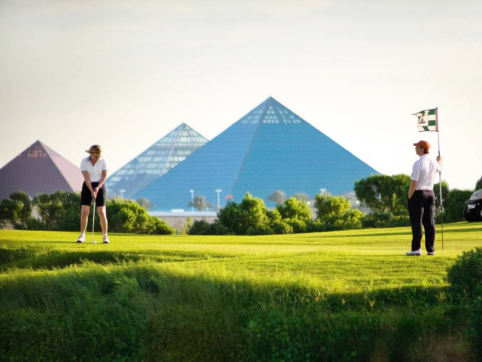 Four people golf on the Moody Gardens Golf Course with the three Moody Gardens pyramids in the distance